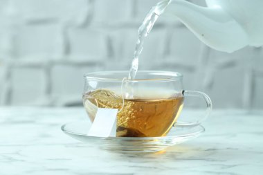 Sıcak suyu fincana dök, çay poşeti açık mermer masaya, yakın çekim.