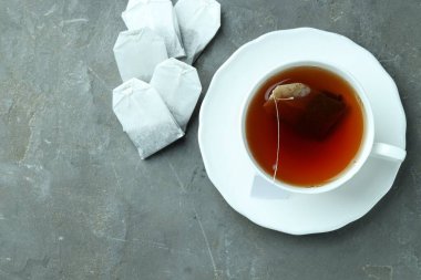 Çay poşetleri ve bardakta sıcak içecek gri desenli masada, düz yerde. Metin için boşluk