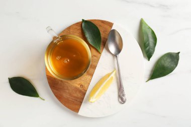 Yeşil çayı fincanda, kaşıkta, yapraklarda ve bir dilim limonu beyaz mermer masada, düz bir şekilde
