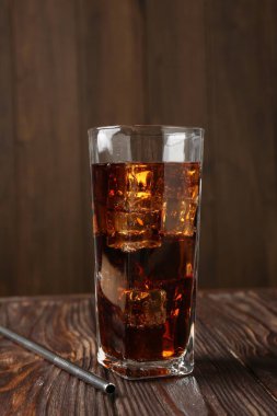 Bardakta buz küpleriyle soğuk kola ve ahşap masada saman içmek.