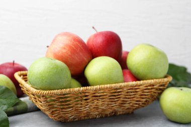 Taze olgun elmalar hasır sepetin içinde Gri masada, yakın plan