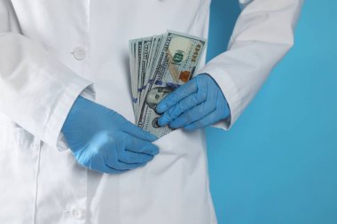 Yozlaşma konsepti. Doktor cebine dolar banknotları koyuyor açık mavi arka planda, yakın plan