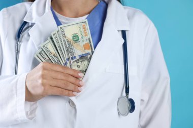 Yozlaşma konsepti. Doktor ceketine açık mavi arka planda dolar banknotları yerleştiriyor.