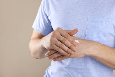 Bej arka planda el kremi süren bir adam, yakın plan. Metin için boşluk