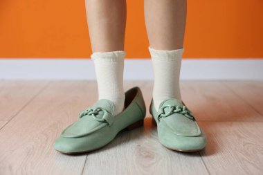 Çocuk turuncu duvarın yanında büyük ayakkabılar giyiyor, yakın plan.