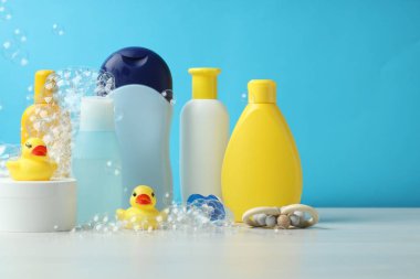 Bebek kozmetik ürünleri, emzik, lastik ördekler ve uçan baloncuklar açık mavi arka plana karşı gri masada