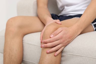 Evdeki kanepede dizinde ağrıdan muzdarip genç adam, yakın plan.