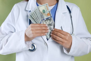 Yozlaşma konsepti. Doktor yeşil arka planda ceketine dolar banknotları koyuyor.