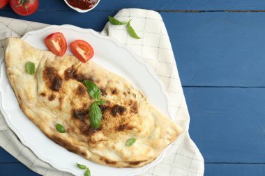 Fesleğenli, domatesli ve mavi ahşap masadaki soslu leziz bir calzone. Metin için boşluk