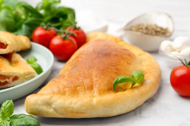 Domatesli lezzetli vejetaryen calzone, mozzarella peyniri ve beyaz mermer masada baharatlar, yakın plan.