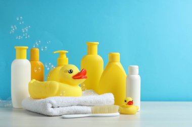 Bebek kozmetik ürünleri, plastik ördekler ve gri masada açık mavi arka planda uçan baloncuklar. Metin için boşluk