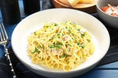 Lezzetli makarna Carbonara mavi ahşap masada servis edilir, yakın plan.