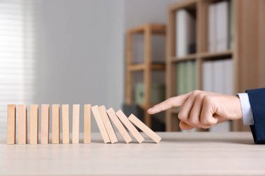 Domino etkisi. Masada tahta blokları iten adam, yakın plan.