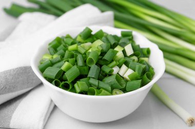 Kavanozda doğranmış yeşil soğan ve sapları beyaz masada, yakın plan.