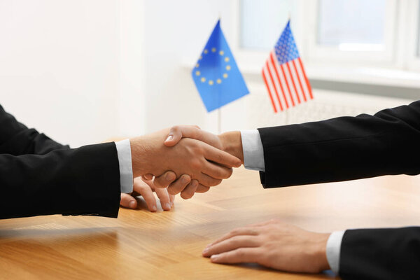Diplomats shaking hands during meeting at wooden table indoors, closeup