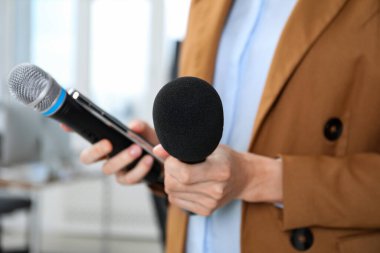 Kapalı mekanda mikrofonları ve akıllı telefonu olan bir gazeteci.