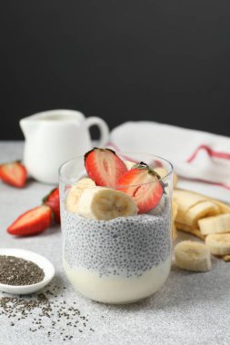 Çilekli lezzetli chia pudingi ve açık gri masada cam içinde muz.