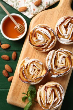 Yeşil ahşap masada servis edilen pudra şekerli lezzetli elma gülleri.