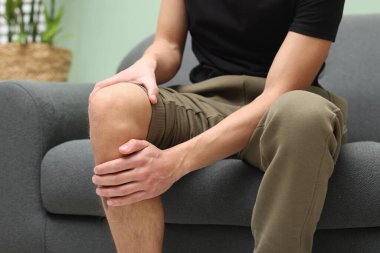 Evdeki kanepede dizinde ağrıdan muzdarip genç adam, yakın plan.