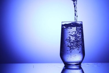 Serinletici gazoz suyunu mavi arka planda cama döküyorum, yakın plan. Metin için boşluk