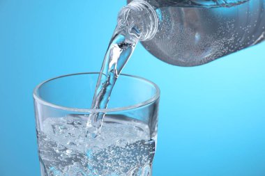 Açık mavi arkaplanda şişeden cama taze soda dökülüyor, yakın plan.
