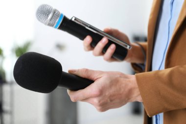 Kapalı mekanda mikrofonları ve akıllı telefonu olan bir gazeteci.