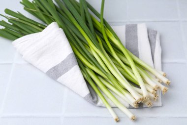 Taze yeşil soğanlar beyaz fayanslı masada, yakın plan.