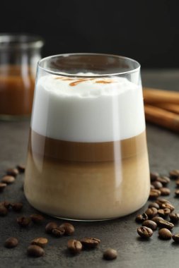 Bardakta latte macchiato, kahve çekirdekleri ve tarçınlı gri masa, yakın plan.