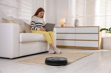 Evde dizüstü bilgisayarı olan genç kız, robotik elektrik süpürgesine odaklan.