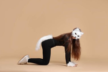 Quadrobics. Girl wearing cat mask, gloves and tail on beige background clipart