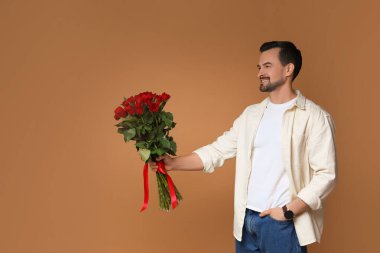 Sevgililer Günün kutlu olsun. Kahverengi arka planda gül demeti olan yakışıklı bir adam.