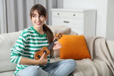 Evdeki kanepede ukulele çalan mutlu kadın.