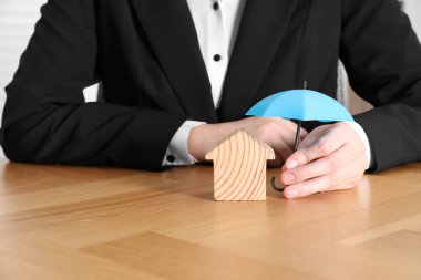 Emlak sigortası. Emlakçı, ahşap ev figürünün üstünde küçük bir şemsiye tutuyor.