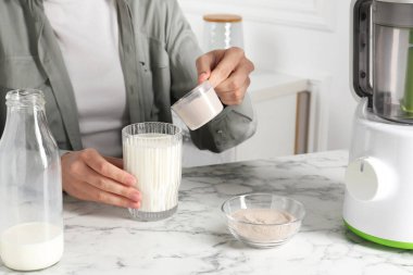 Protein kokteyli yapıyorum. Beyaz mermer masada sütlü bardağa toz ekleyen kadın, yakın plan.