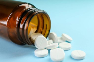 Açık mavi arka planda bir şişe antibiyotik hapı, yakın plan.