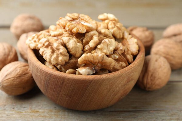 Peeled walnuts in bowl and whole ones on wooden table, closeup