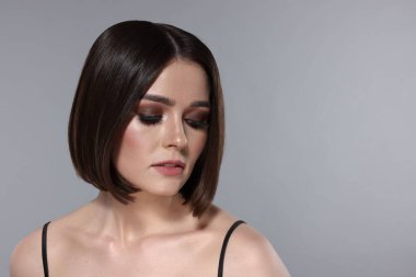 Açık gri arka planda muhteşem düz saçları ve şık makyajı olan güzel bir genç kadının portresi.