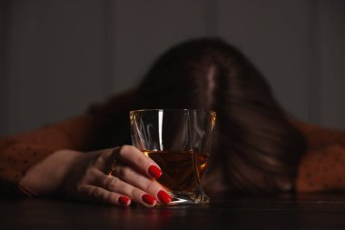 Alkol bağımlılığı. Ahşap masada bir bardak viskisi olan kadın, seçici bir odak noktası.