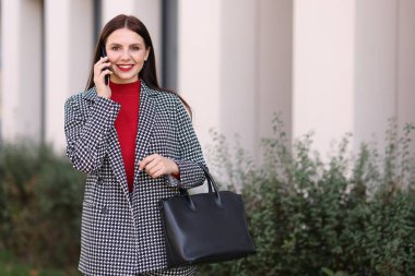 Şık takım elbiseli güzel bir kadın dışarıda akıllı telefondan konuşuyor. Metin için boşluk