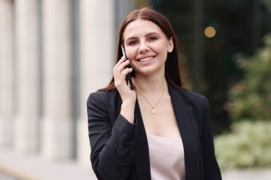 Şık takım elbiseli bir kadın dışarıda telefonla konuşuyor.
