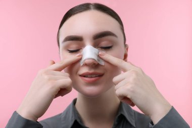 Pembe arka planda estetik ameliyat sonrası burnu bandajlı bir kadın.