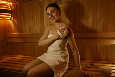 Saunada bankta masaj süngeri olan bir kadın.