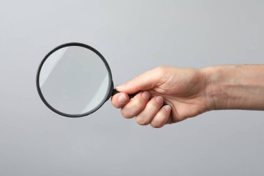 Gri arka planda büyüteç tutan kadın, yakın plan. Anahtar sözcük kavramını bul