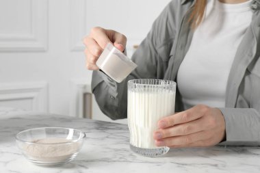 Protein kokteyli yapıyorum. Beyaz mermer masada sütlü bardağa toz ekleyen kadın, yakın plan.