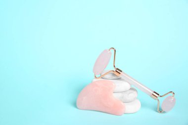 Gül kuvars yüz silindiri, gua sha aracı ve açık mavi arka planda spa taşları. Metin için boşluk