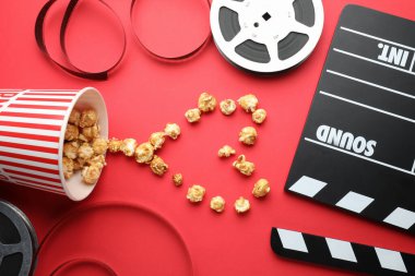 Film alkışı, tatlı patlamış mısır ve kırmızı arka planda film makaraları, düz konum