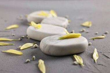Gri masadaki spa taşları, çiçekler ve yapraklar, yakın plan.