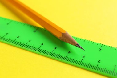 Sarı arkaplanda cetvel ve kalem, yakın plan