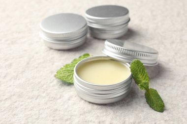 Mint lip balms and green leaves on beige textured table, closeup. Cosmetic product clipart