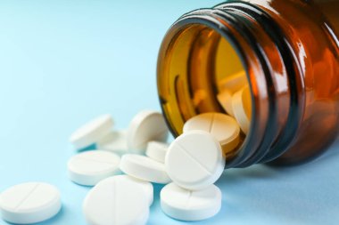 Açık mavi arka planda bir şişe antibiyotik hapı, yakın plan.